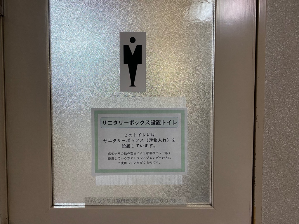 このトイレにはサニタリーボックス（汚物入れ）を設置しています。のお知らせが貼られたトイレの扉の写真