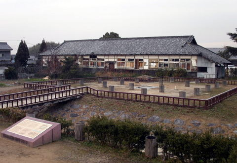 横に長い建物の前に茶色の低い柵で囲われた円柱の石が複数置かれている広場の写真