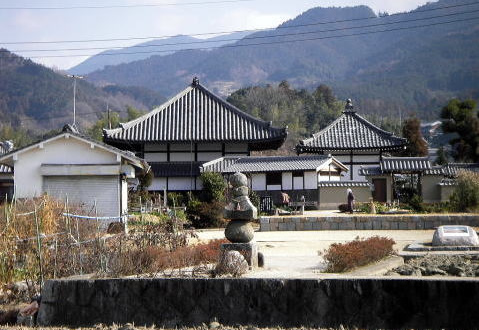 石の塚の向こうにある黒い瓦屋根の飛鳥寺とその奥に山々が広がっている様子の写真