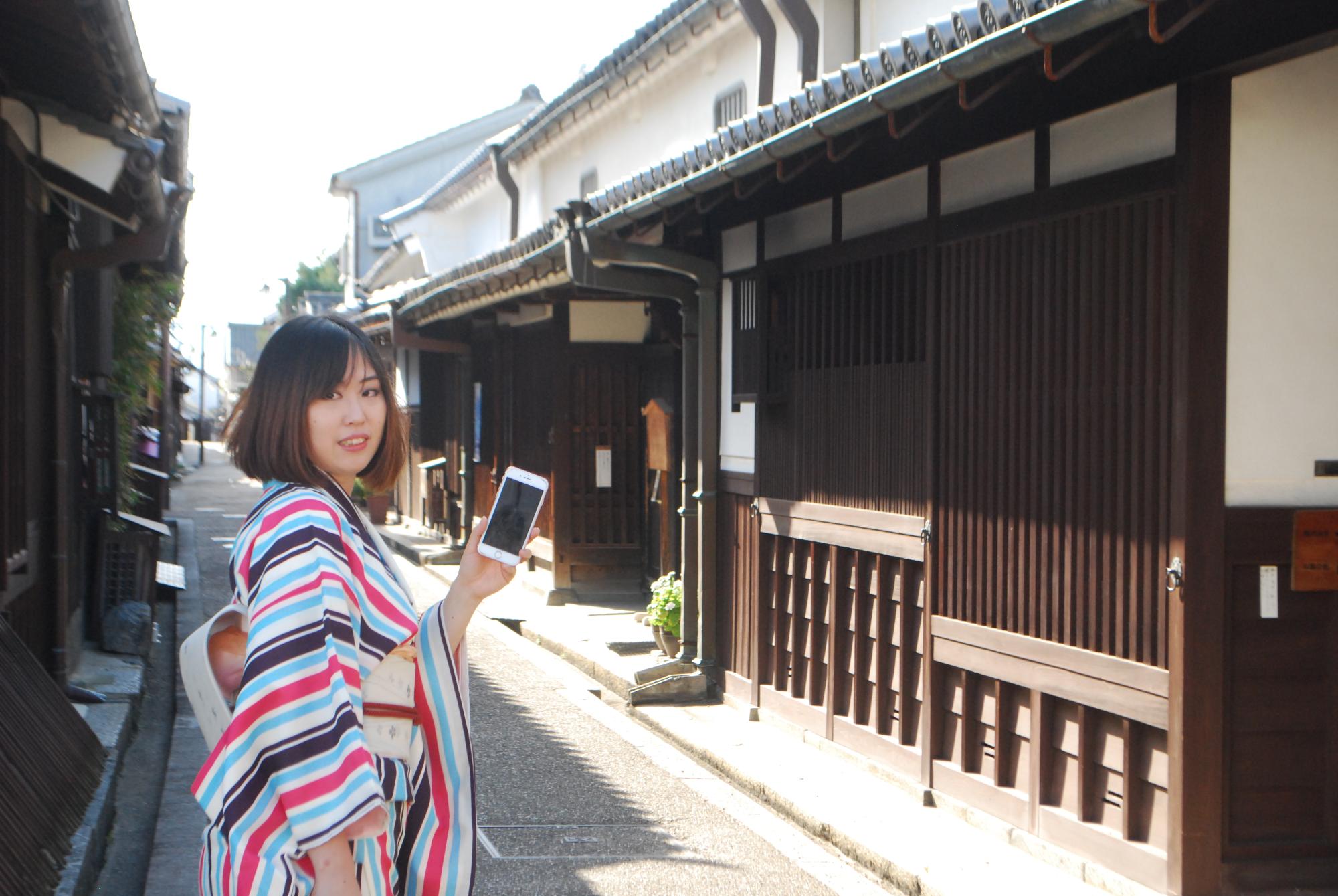 古い街並みの中でスマートフォンを持っているカラフルな着物を着た女性の写真