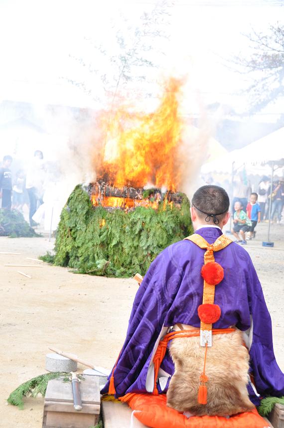 本薬師寺跡で木を組んで火を焚き、その前で紫色の法衣を着た人が座っている様子の写真
