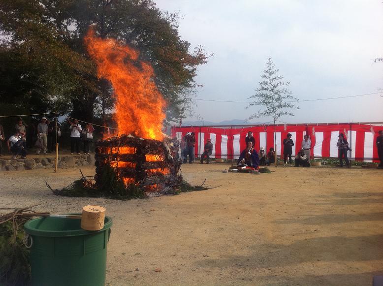 紅白の幕が張られた本薬師寺跡で木を組んで焚いた火が燃え盛り、それをたくさんの人たちが見届けている様子の写真