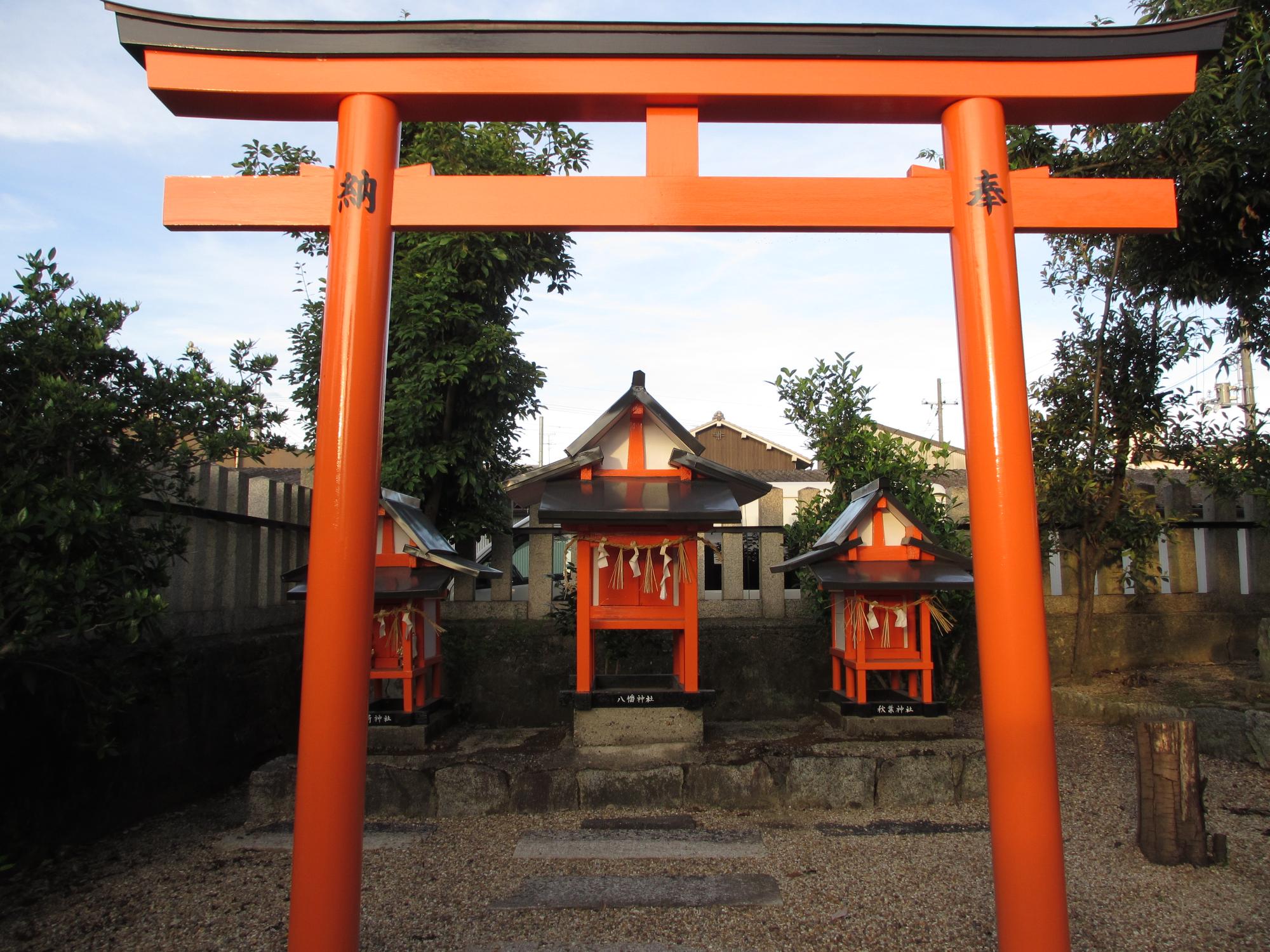 朱色の鳥居の向こうに朱色に黒い屋根の小さいお社が3つ並んでいる写真