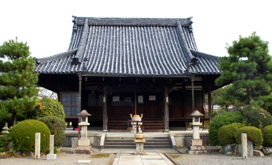 左右に丸い低木と植木、石造りの灯籠が置かれたお寺の全体が見える写真