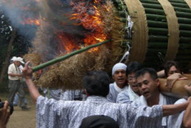 たくさんの男性が担いでいる火が付いたたいまつの中にひとりの男性が竹の棒をさしている写真
