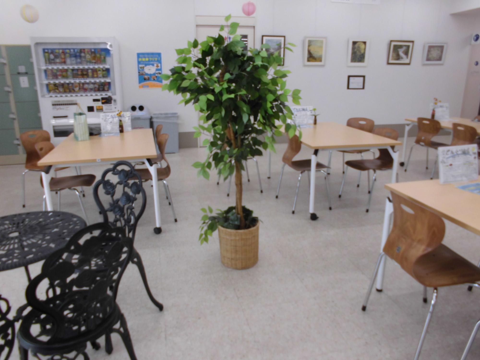 中央に観葉植物が置いてあり周りにテーブルとイスが設置されている休憩スペースの写真