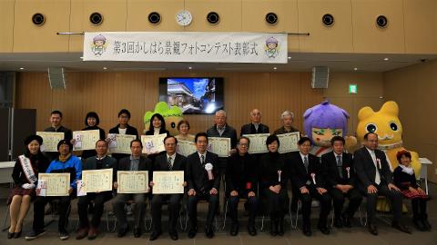 市長や関係者たちと受賞者たちが表彰状を掲げながら写っている集合写真