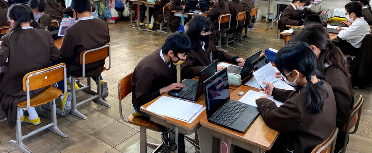 向かい合うように机を突き合わせて座る生徒たちがノートパソコンを操作して学ぶ様子