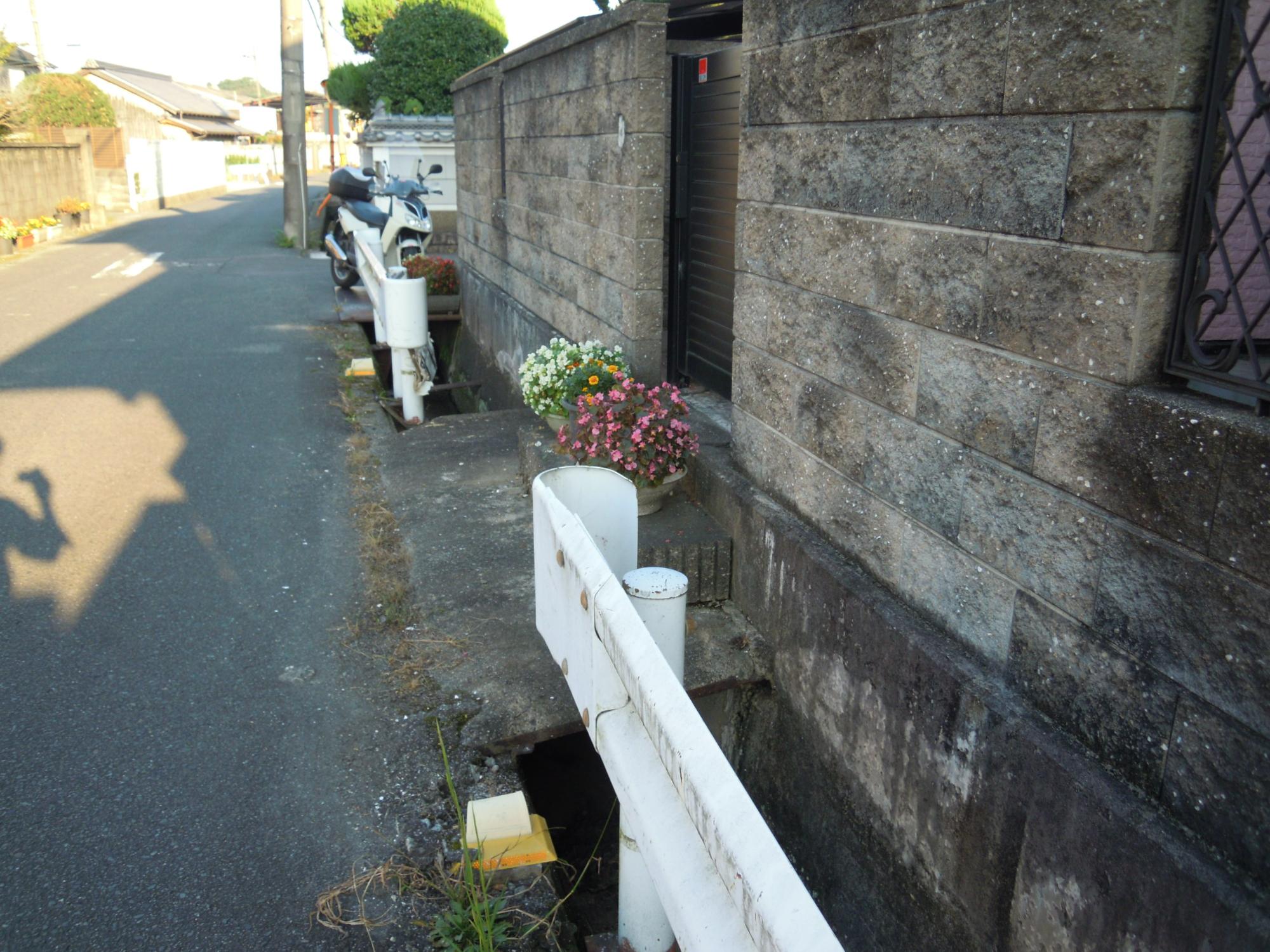側溝の橋の上にある赤色と白色の花が咲いている植木鉢2個の写真