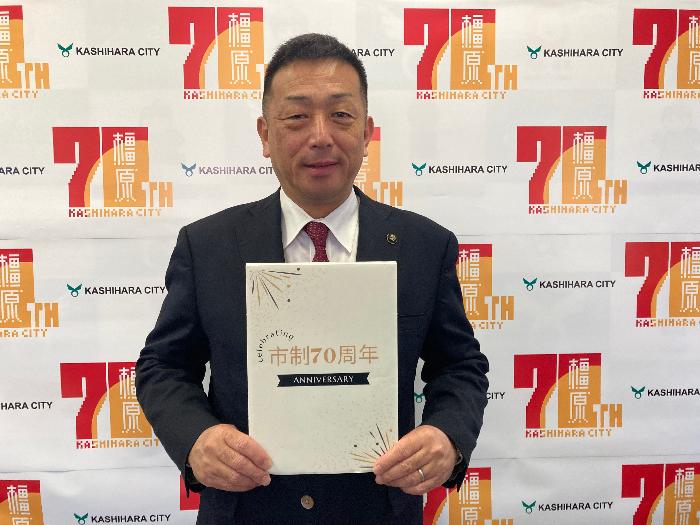 市政70周年の掲示ボードを手に持つ亀田市長の写真