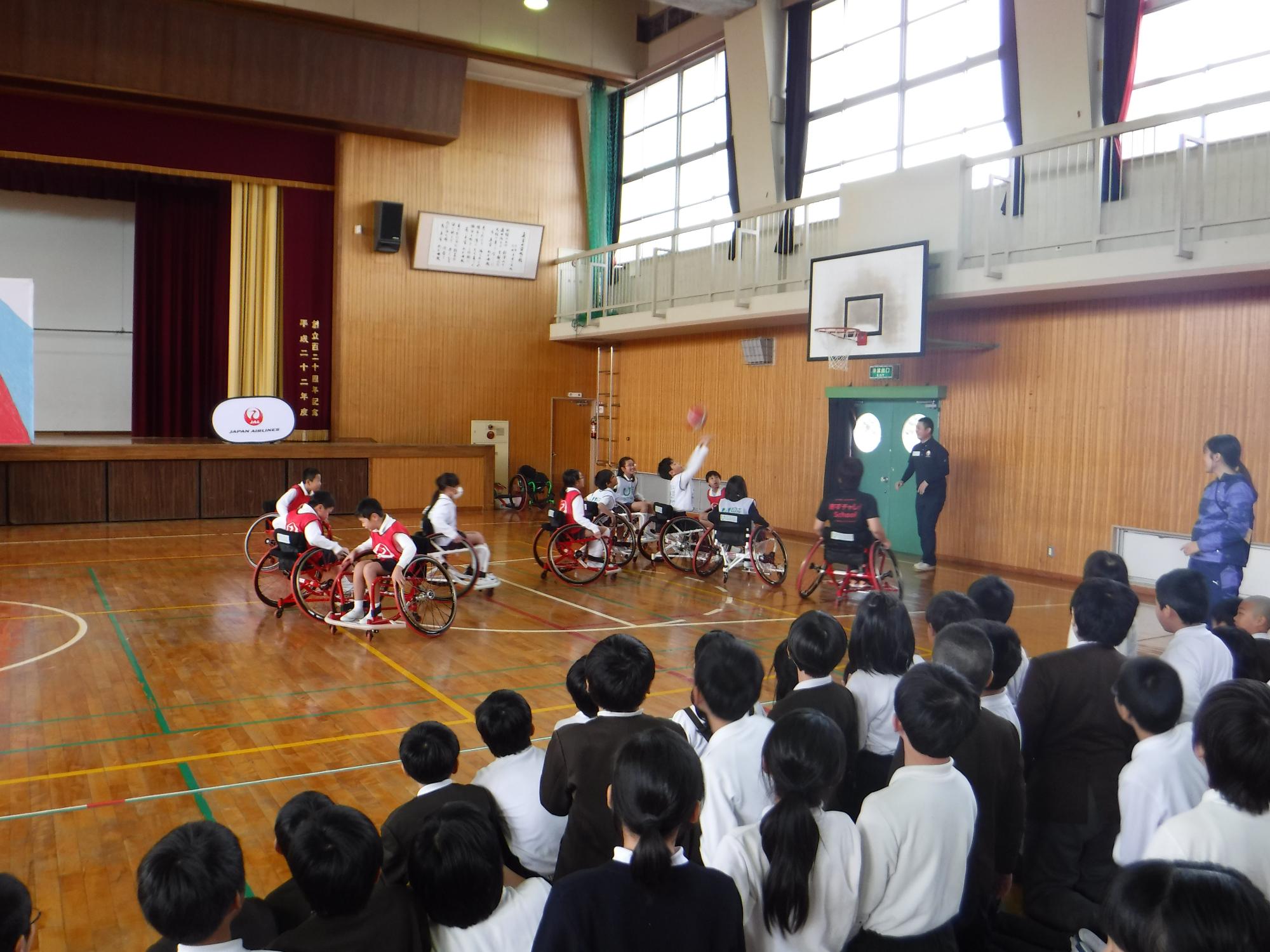 車いすバスケットボールをしている小学生たちのうち、白のユニフォームを着た一人がシュートをしている写真