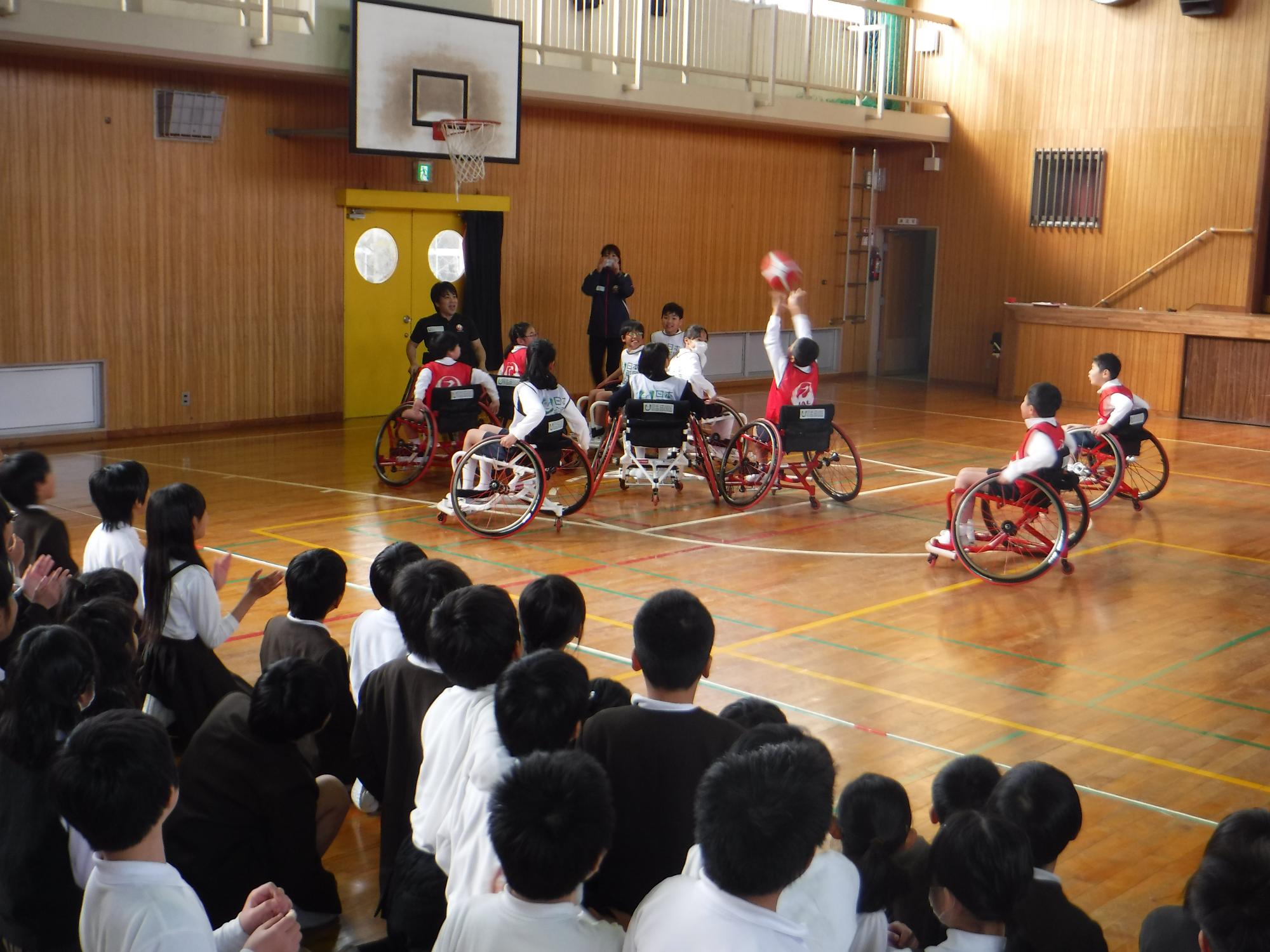 車いすバスケットボールをしている小学生たちのうち、赤のユニフォームを着た一人がシュートをしている写真