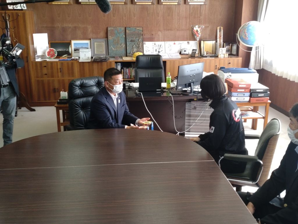 互いにテーブルの椅子に座り向かい合い、メダルを手にする亀田市長（左）と新添選手（右）の写真