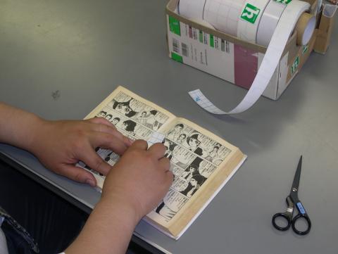 グレーの机の上でテープを使って漫画本を修理している様子の写真