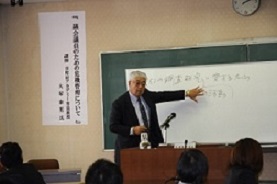 ホワイトボードに手をかざしながら講演を行う大塚康男氏の写真