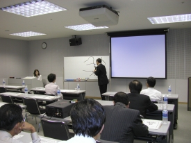 ホワイトボードを指しながら講義を行う山田勝久氏の写真