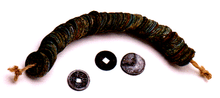 一本の紐に、円形の古い貨幣が何枚も通されたものと、その手前に、中心に四角い穴が開いた古い貨幣が3枚置かれている写真。