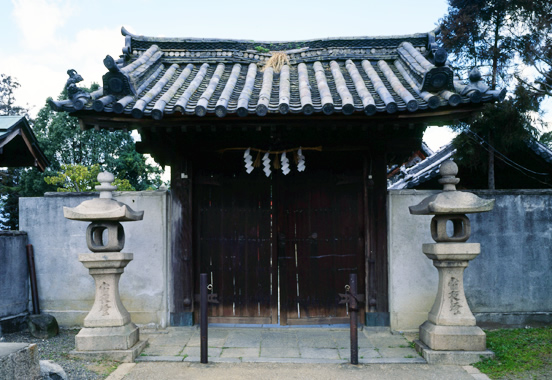 石造りの灯籠が左右に設置されている、寺の木造の門の写真