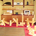 和風の内装の部屋に木製の四角い形状のものが展示されている写真