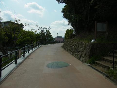 右側に木々の生い茂る石垣と階段が見える道路の写真