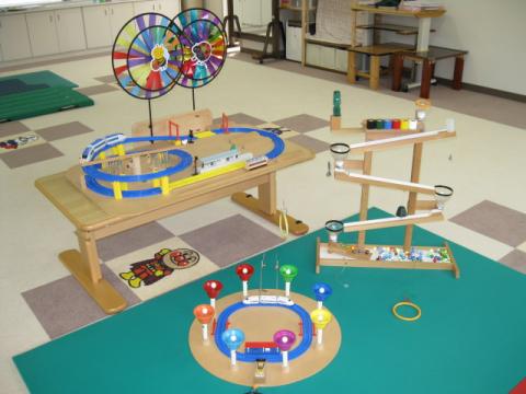 緑色のマットやミニテーブルの上に複数のおもちゃが置かれた機能訓練室内の写真