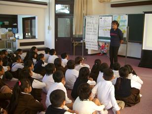 黒板の前に立っているフィリピン人講師と彼から授業を受けている小学生たちの写真
