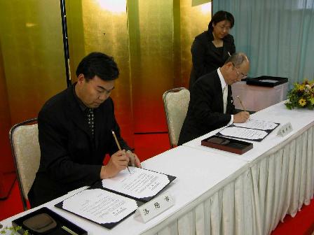 二人の男性が座って認定書にサインを書いている写真