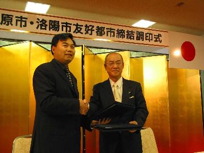 金屛風の前で二人の男性が握手をしている写真