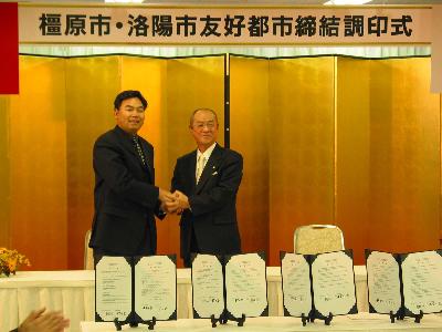 二人の男性が協定書・協議書の後ろで握手をしている写真