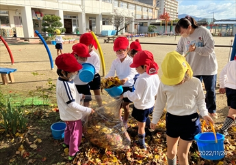 園庭で園児が落ち葉拾いを楽しんでいる写真