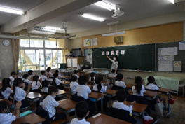 低学年の児童たちが先生が示した黒板の方を向きながら授業を受けている写真