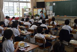 低学年の児童たちが先生と一緒に給食を食べている写真