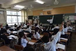 低学年の生徒たちが先生の質問に対して手を挙げているときの写真