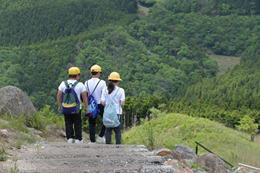 緑色の山を背景に5年生の生徒3人が登山道を歩いている写真