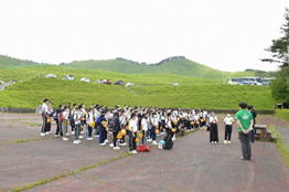 緑色に見える山々を背景に5年生の生徒たちが整列しているときの写真