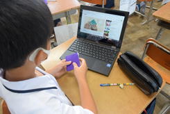 男子生徒がパソコンを見ながら折り鶴を折っている写真