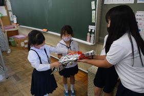 6年生の女子生徒が1年生の女子児童2人に手作りメダルをプレゼントしている写真