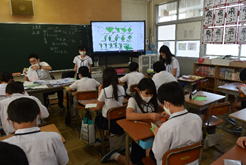 教室のモニターに折り鶴の折り方を表示させながら子どもたちが折り鶴を折っている写真